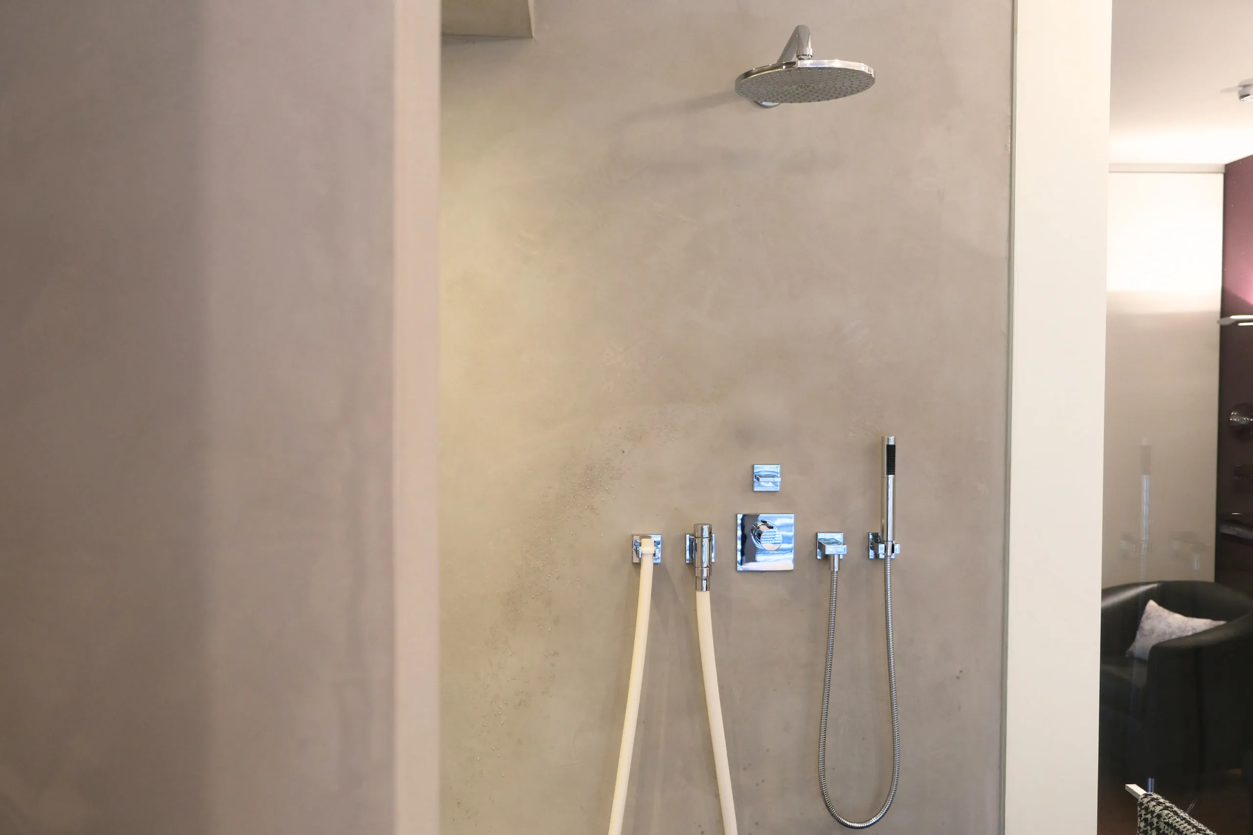 Regendusche an fugenloser grauer Wand mit Armatur und Handbrause