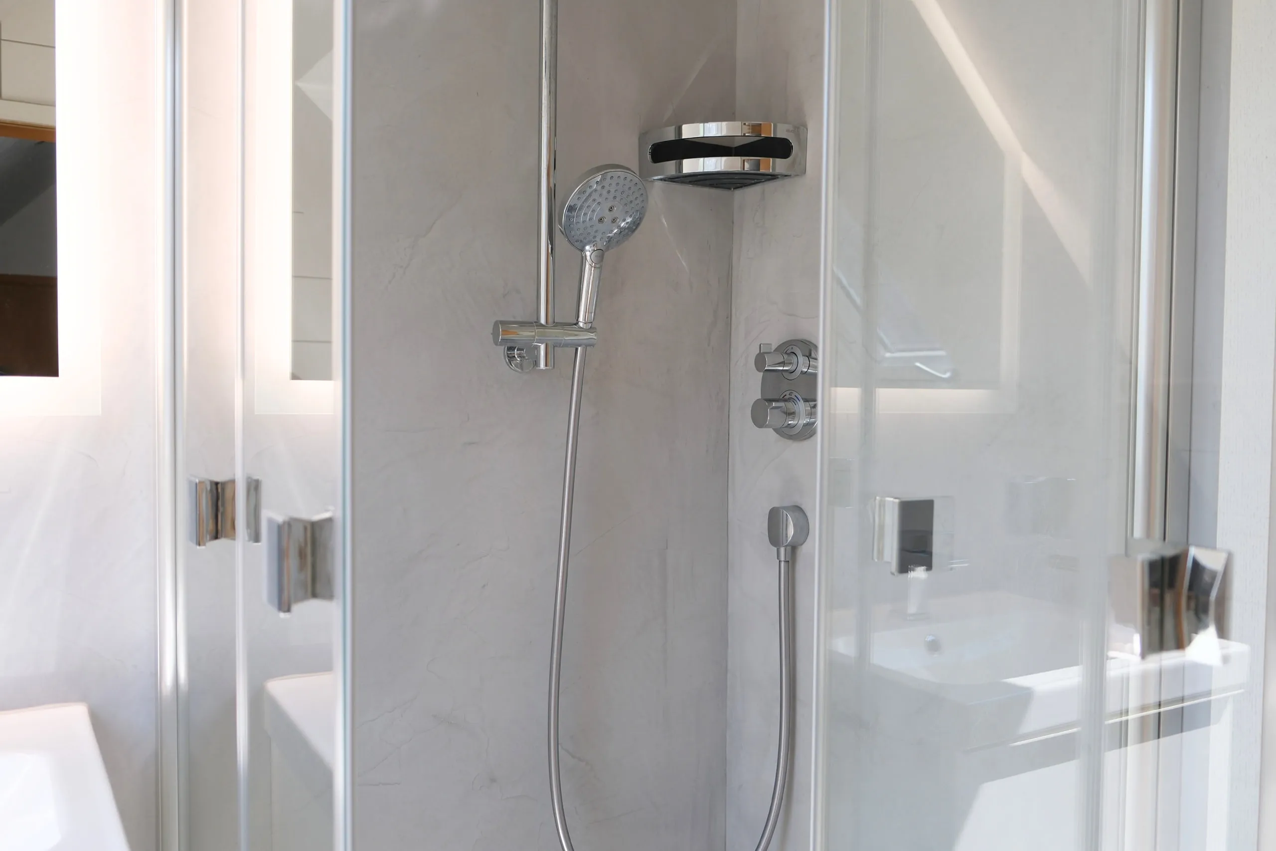 Dusche hinter Glastüren mit Handbrause und fugenloser Wandfläche