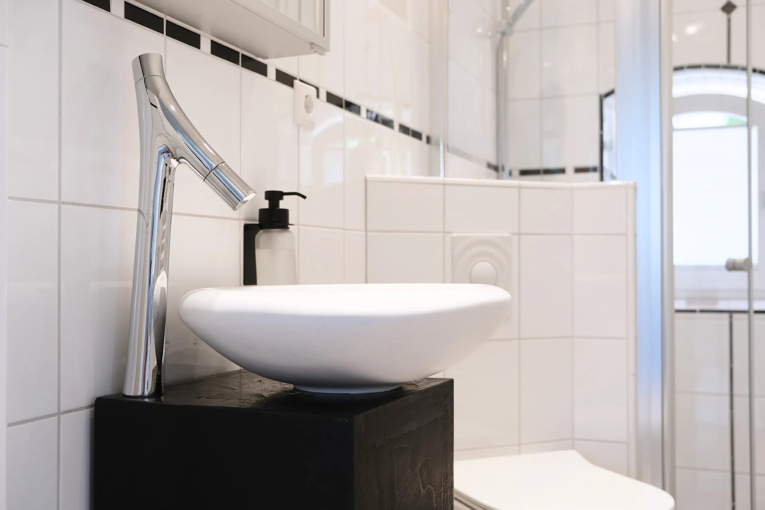 Aufsatzwaschtisch auf dunklem Sockel mit Armatur, dahinter die Dusche