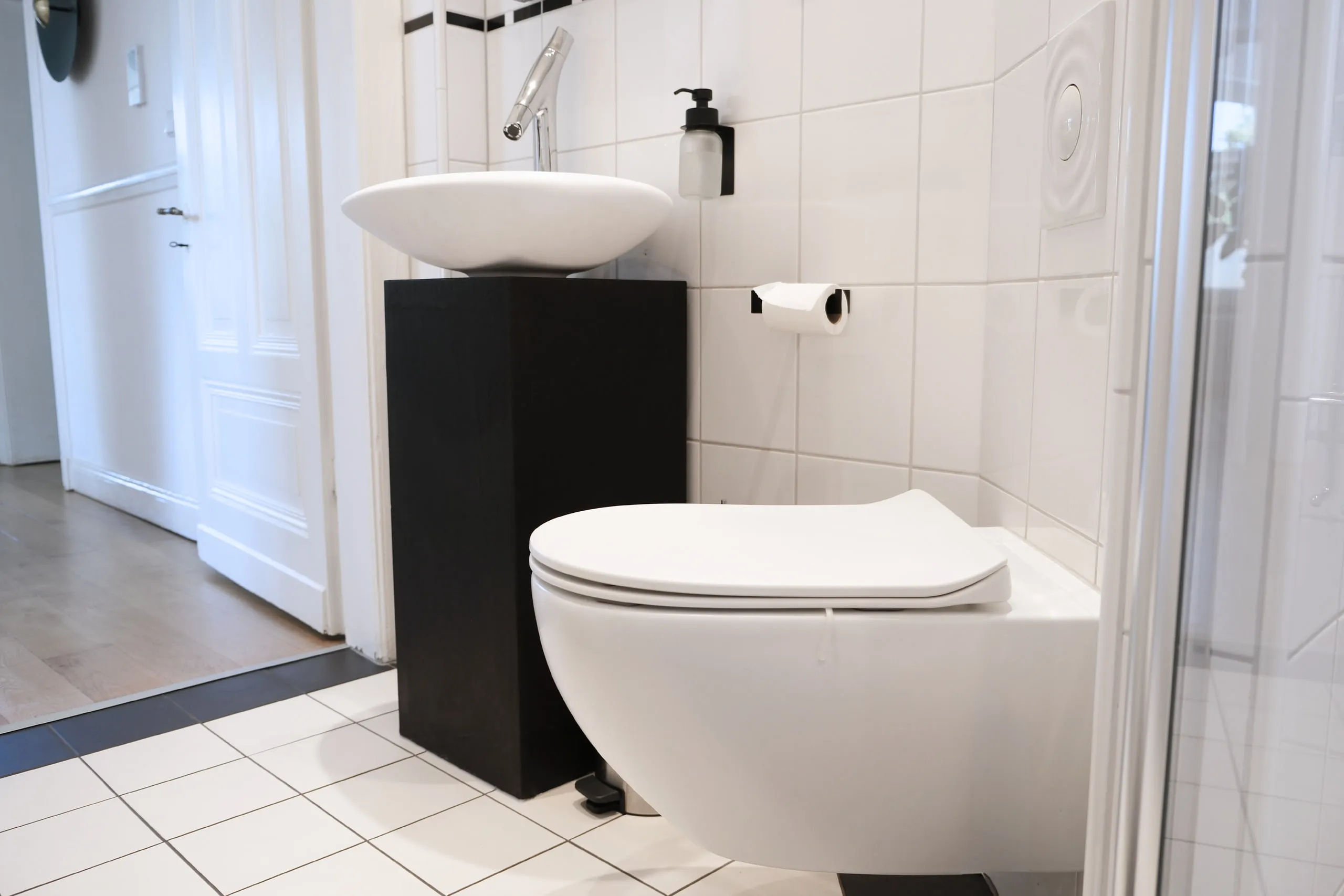 Waschtisch auf Sockel und wandhängendes WC, im Hintergrund die Badezimmertür