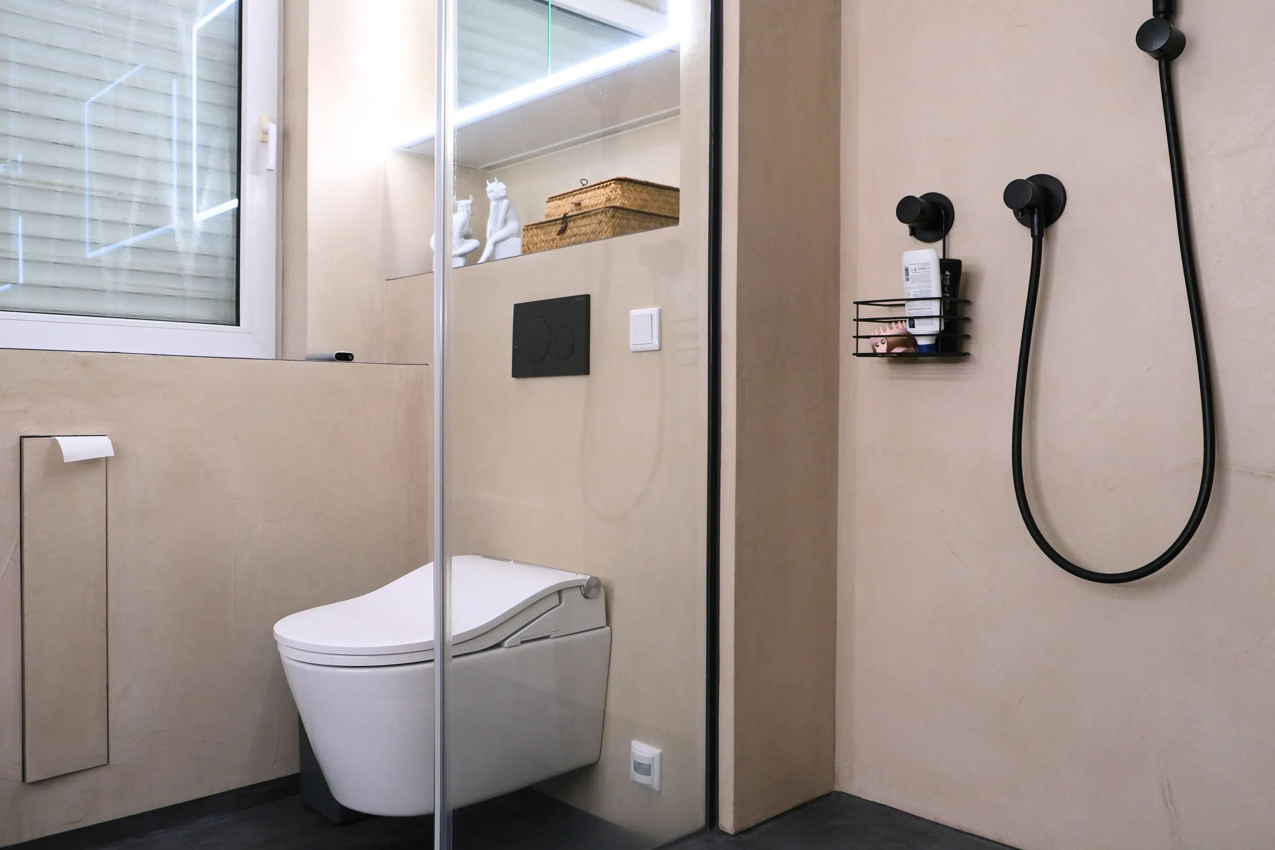 Dusch-WC neben der Dusche mit schwarzer Handbrause und Fenster