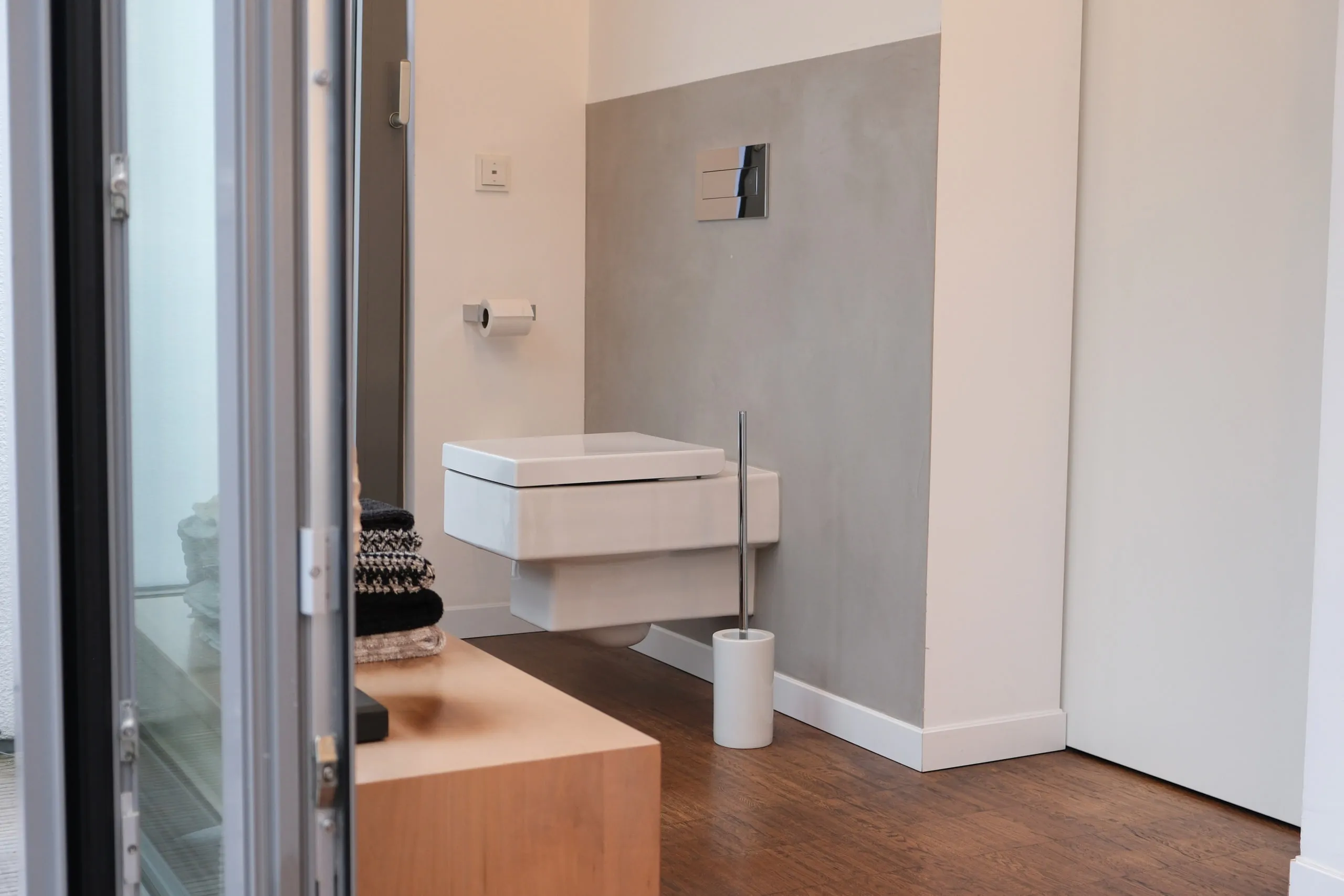 Wandhängendes WC an fugenloser grauer Wand, davor ein Holzboden