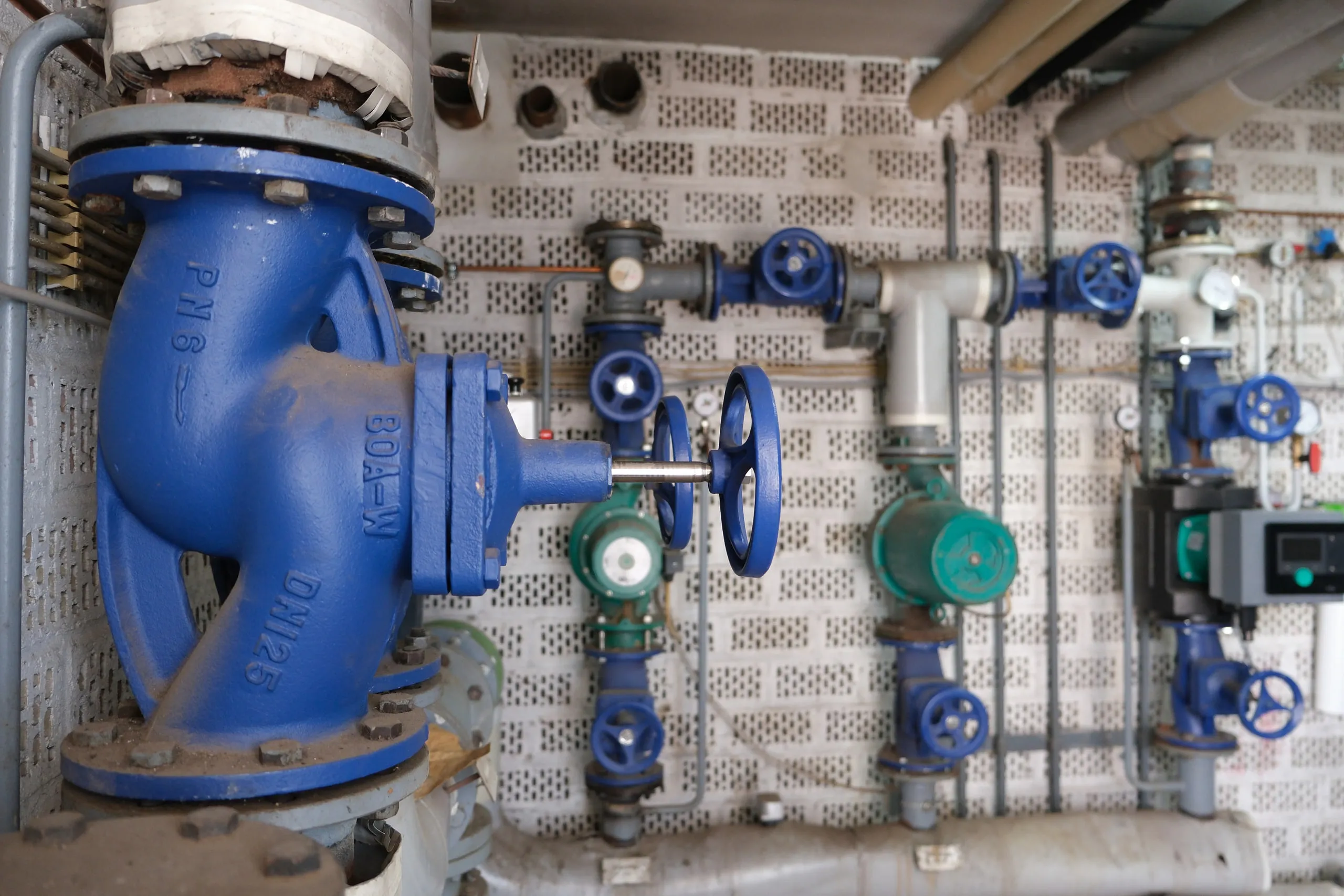 Heizzentrale mit großer blauer Absperrklappe, Armaturen und Umwälzpumpen