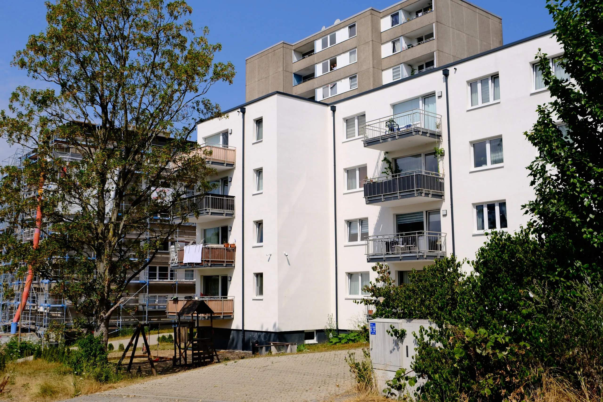 Wohnhaus in Herms mit Balkonen, dahinter ein höheres Gebäude