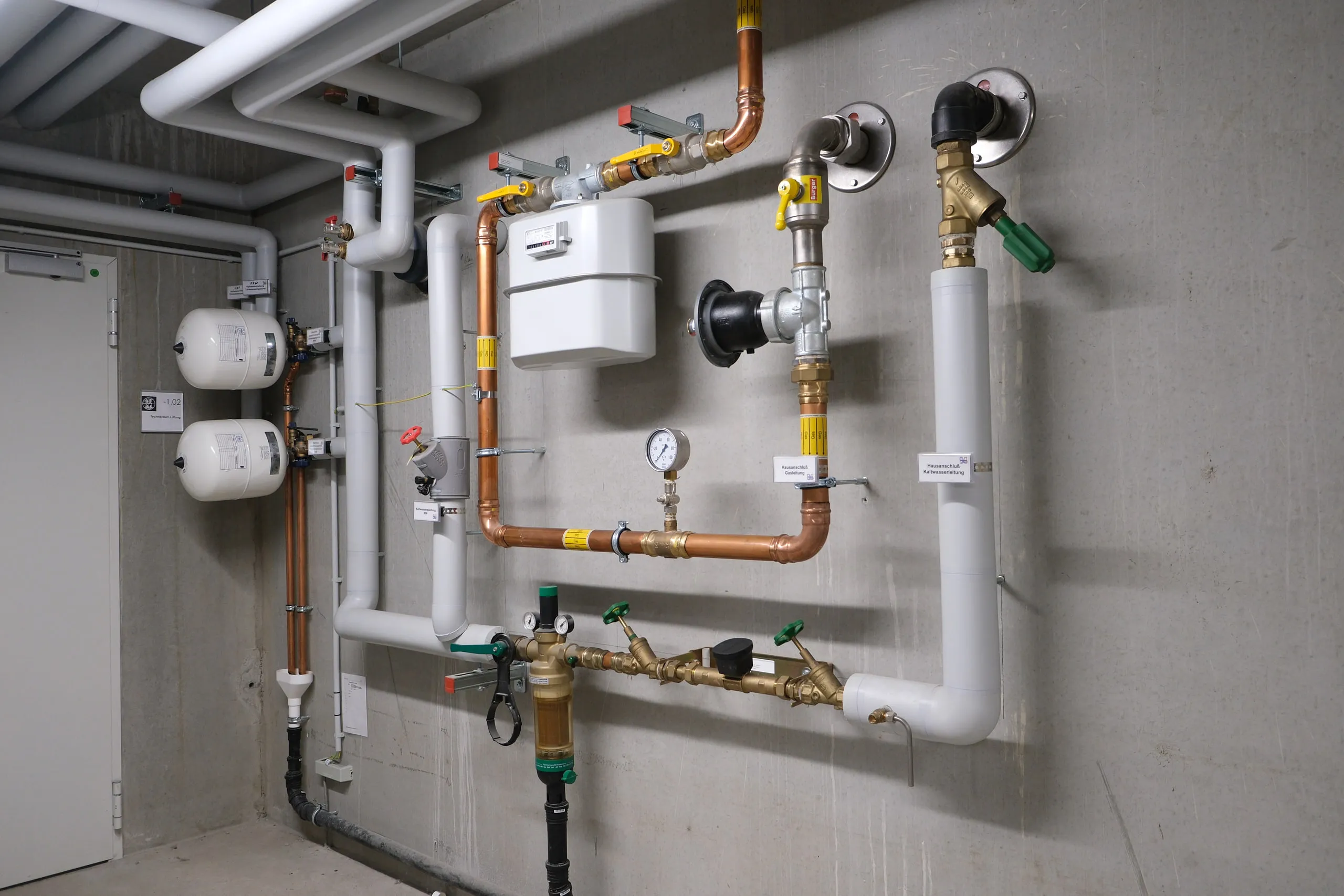 Gaszähler mit Kupfer- und Gasleitungen an der Wand eines Technikraums