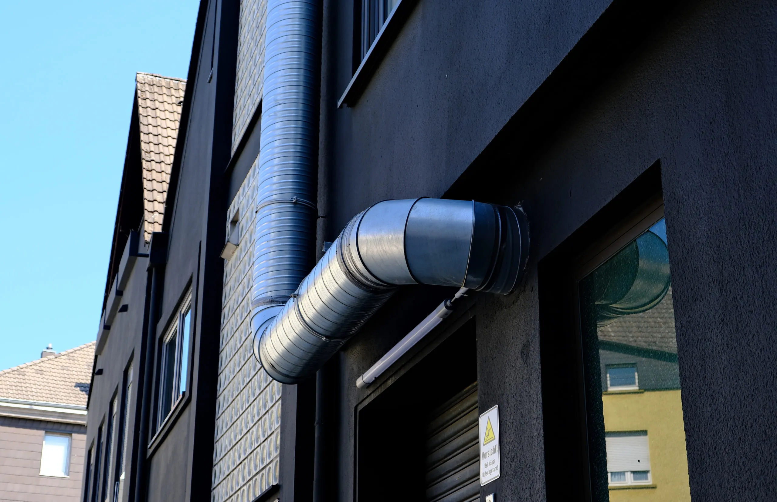 Außen geführter Lüftungskanal an einer dunklen Fassade