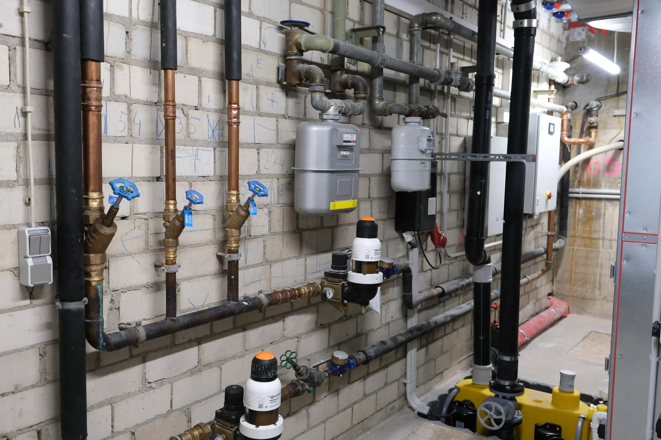 Technikraum mit Gaszählern, Wasserzählern und Rohrleitungen an der Wand