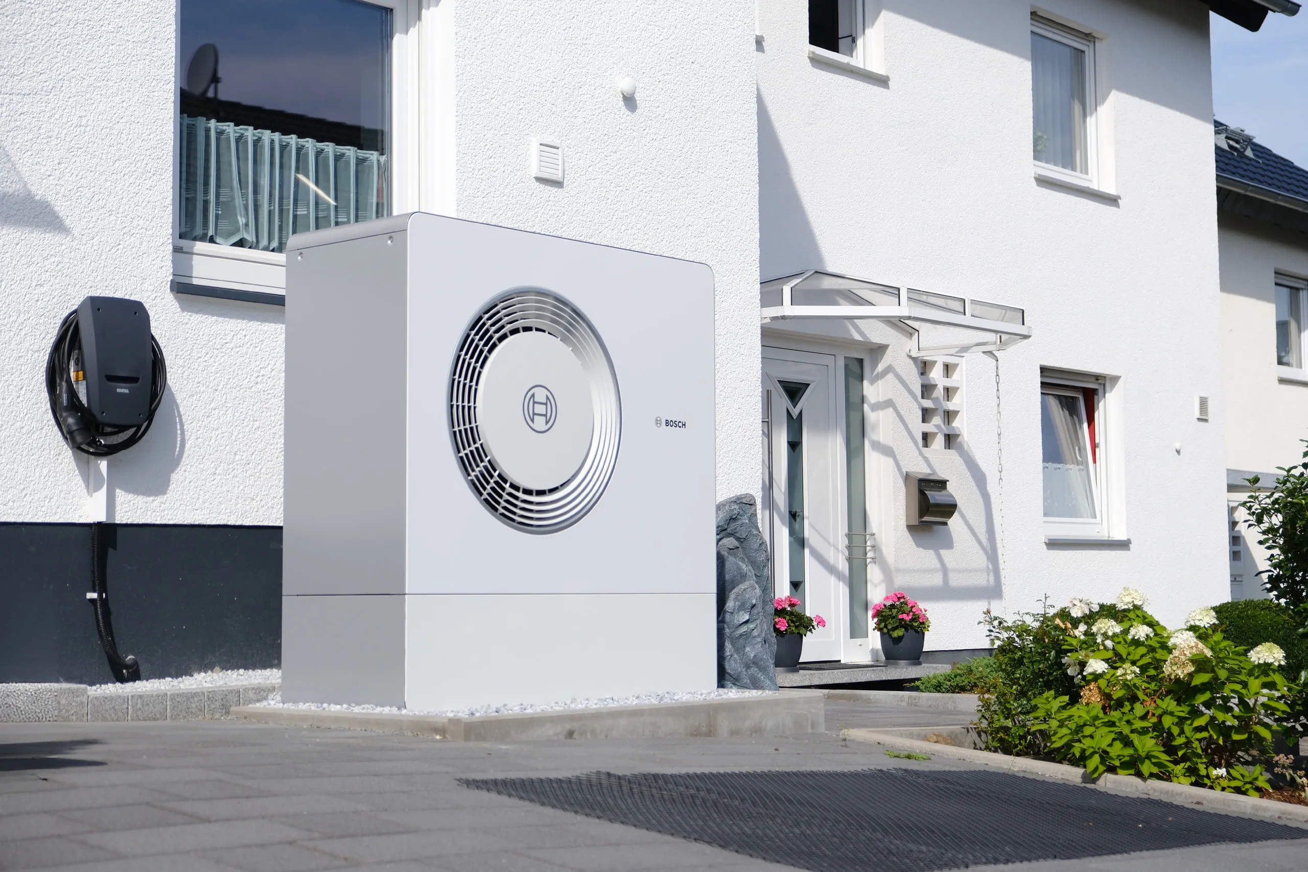 Bosch-Wärmepumpe vor einem Einfamilienhaus, daneben eine Wallbox